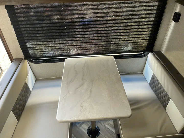 Interior of an RV rental: dinette area with light table, plush gray and white booth seating, and pleated window blinds.. Forest River Salem 179 2021