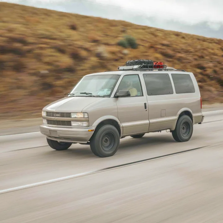 Light gray modified van, with roof rack & gear, speeding on highway. Perfect RV rental for adventure road trips.. Chevrolet Astro Van AWD 2003