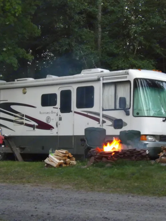 Experience an RV rental: a white Allegro Bay motorhome is set up at a campsite with a lively campfire and chairs.. Tiffin Motorhomes Allegro Bay 2001