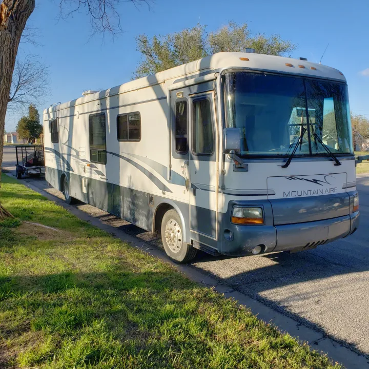 Large cream and gray Mountain Aire motorhome for RV rental. Parked on asphalt beside green grass under a clear sky.. Newmar Mountain Aire 1998
