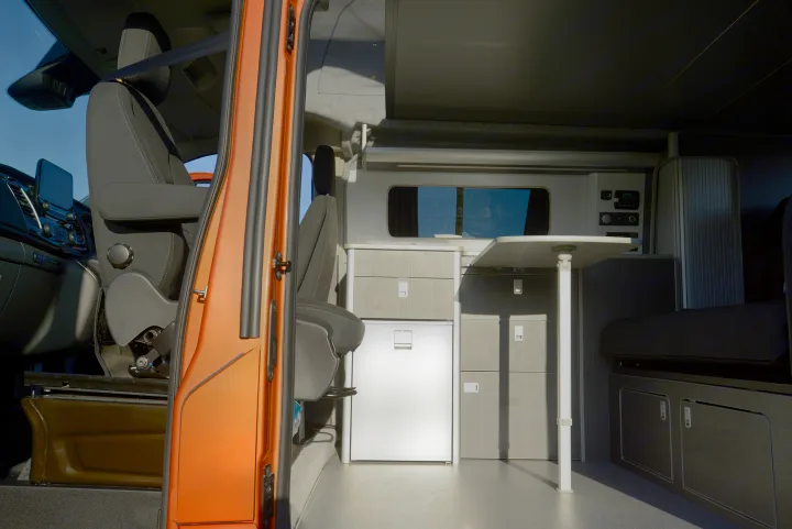Step into this RV rental camper van: A modern interior featuring front seats, kitchen, dining table, and sofa area.. Ford Custom 2018