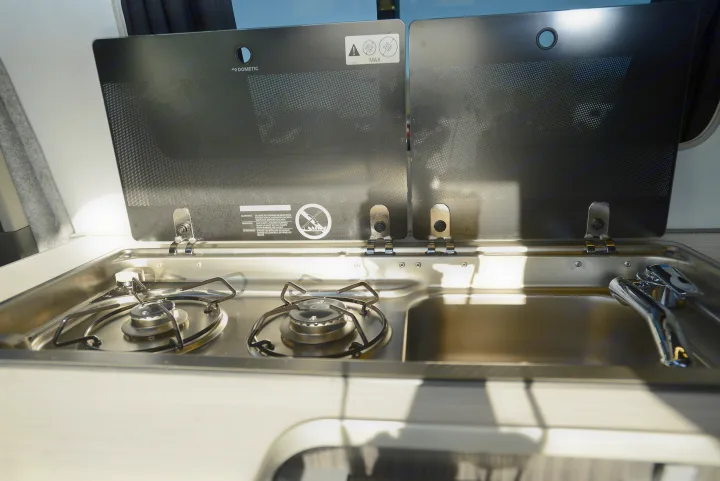 Compact kitchen in an RV rental with a two-burner stove and sink, ready for adventure cooking. Dometic brand.. Ford Custom 2018