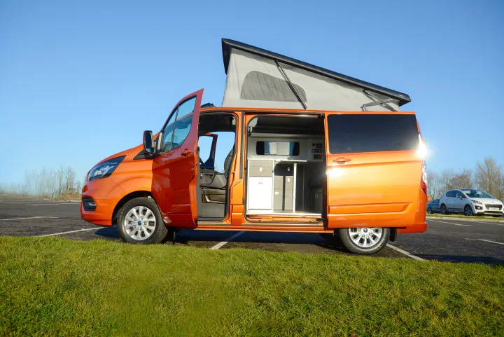 Vibrant orange pop-top camper van, an ideal RV rental, with open doors revealing its compact interior and amenities.. Ford Custom 2018