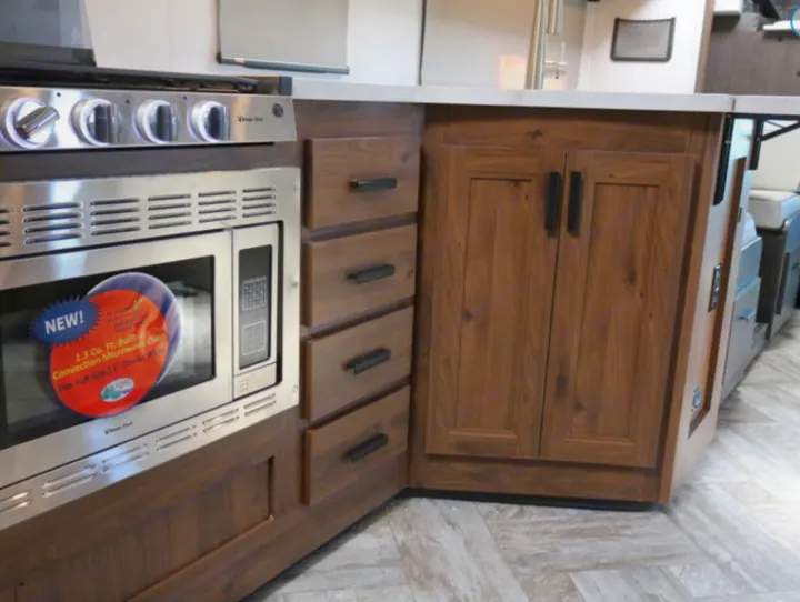 Modern RV rental kitchen with a new stainless steel 1.3 cu ft convection microwave, stovetop, and dark wood cabinets.. Forest River Other 2021