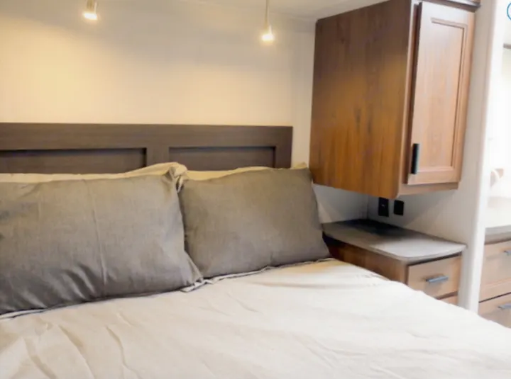 Comfortable RV rental bedroom featuring a full bed, built-in headboard, and wood storage cabinets with outlets.. Forest River Other 2021
