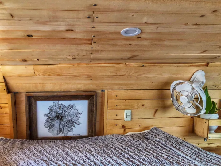 Experience comfort in this RV rental bedroom with wood paneling, a cozy bed, framed art, fan, and plant.. Ford Econoline E250supercab 2006