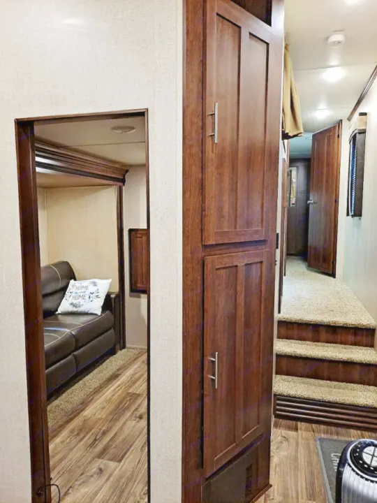 Cozy RV rental interior showing wood floors, a brown couch, tall cabinets, and carpeted steps to a rear hallway.. Keystone Volante 3801MD 2018