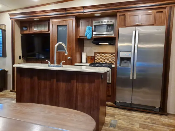 Spacious RV rental kitchen with stainless steel fridge, microwave, gas range, island sink, and TV. Ideal for travels.. Keystone Volante 3801MD 2018