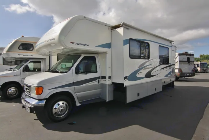 Several white Class C RVs, including a Fleetwood model, parked in an outdoor lot, showcasing options for RV rental.. Tioga M-30u Ford 2005