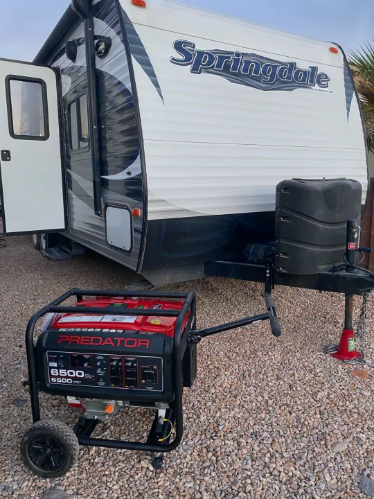 A white Springdale RV rental with open door and a large red Predator generator sits on gravel, useful for camping.. Keystone Springdale 2016