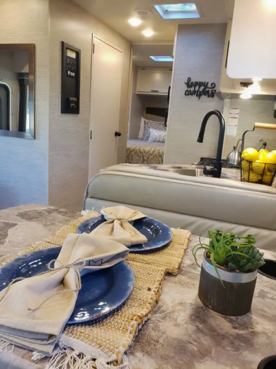 Modern RV rental interior: Kitchen, dining area with blue plates, and a cozy bedroom view.. Thor Four Winds 2021