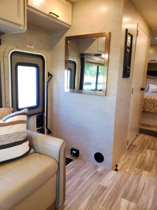Modern RV rental interior, showing living area with couch, door, mirror, and glimpse of the bedroom.. Thor Four Winds 2021