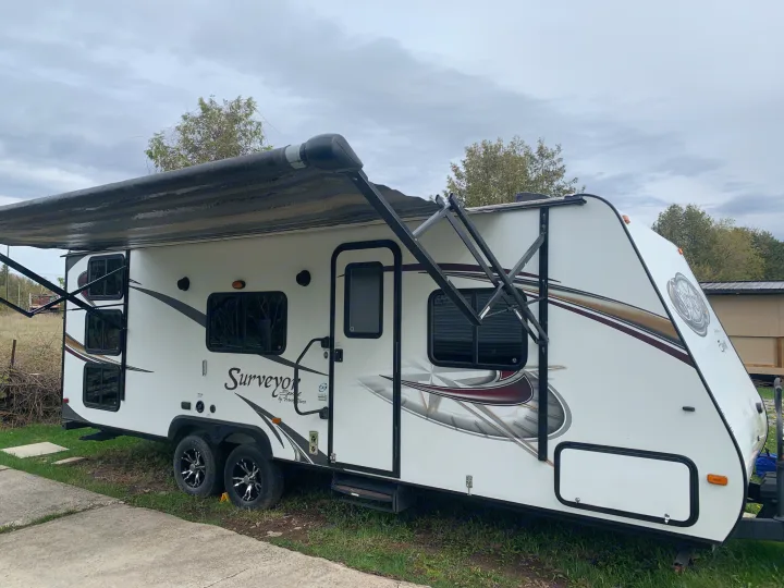 Explore the outdoors with this spacious RV rental. White travel trailer with awning deployed, perfect for your next camping adventure.. Forest River Surveyor Sport 2014