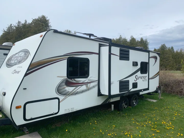 A white Surveyor Sport travel trailer RV, ideal for rv rental, parked on a green lawn with dandelions.. Forest River Surveyor Sport 2014