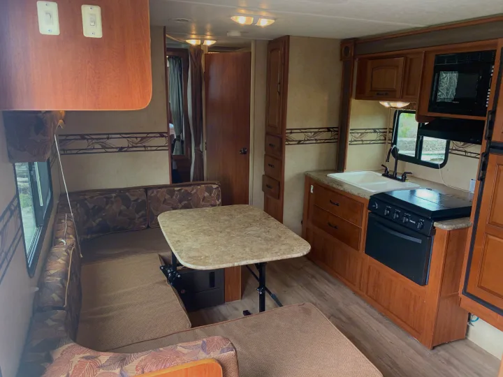 This inviting rv rental features a well-equipped kitchen with stove, sink, & microwave, alongside a comfortable dining booth for camper adventures.. Forest River Surveyor Sport 2014