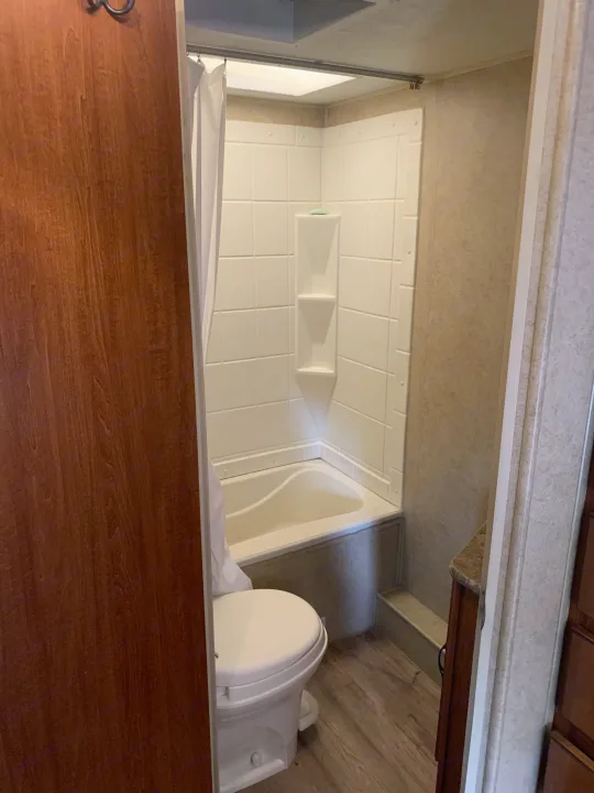 Inside an RV rental: a clean, compact bathroom with a white toilet and corner tub/shower unit. Essential for road trips.. Forest River Surveyor Sport 2014
