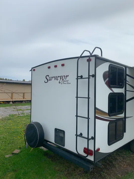 White Surveyor Sport travel trailer, ideal for RV rental, featuring a rear ladder & spare tire. Ready for adventure!. Forest River Surveyor Sport 2014