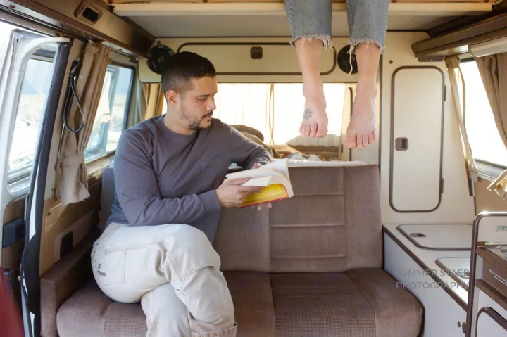 Enjoy leisure in your RV rental! A man reads as bare feet dangle from the bunk in a cozy camper van.. Volkswagen Westfalia 1986