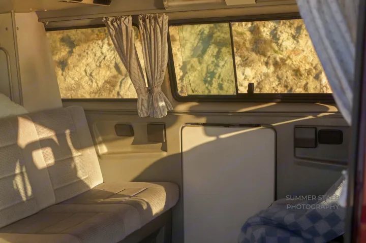 Inside a cozy RV rental: sunlight streams into the camper van, revealing a sunny, rocky landscape outside.. Volkswagen Westfalia 1991