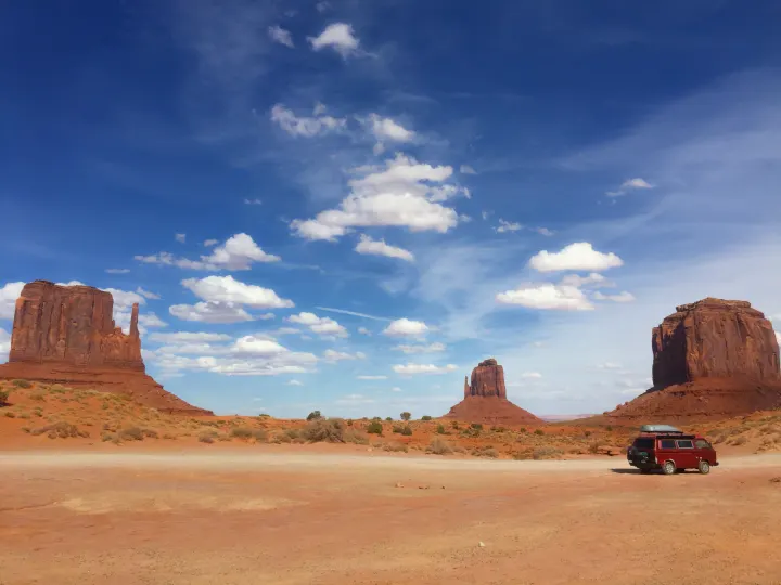 Red RV rental camper van parked in Monument Valley desert with majestic mesas under a blue sky.. Volkswagen Westfalia 1987