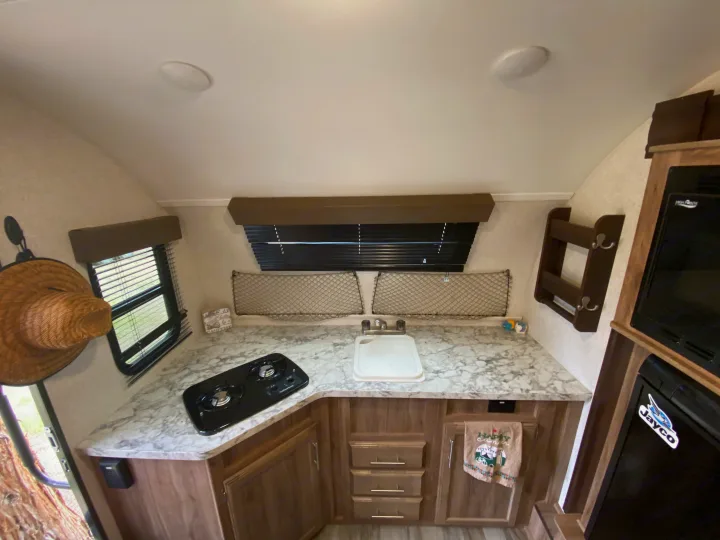 Inside an RV rental: a compact kitchen with a two-burner stove, sink, refrigerator, and microwave for convenient camping.. Jayco Baja 2018