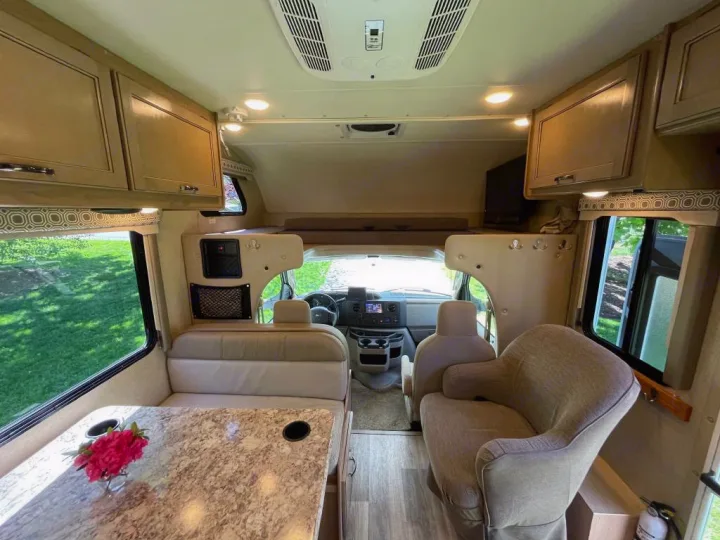 This spacious RV rental interior shows a modern motorhome living area with a dinette, seating, and overhead bunk. Ideal for travel.. Thor Motor Coach Four Winds 2019