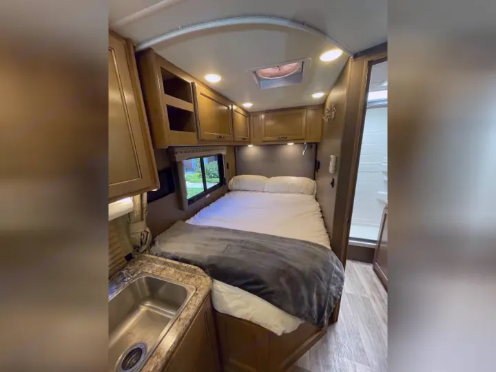 RV rental interior: cozy bed, compact kitchen with sink, and private bathroom access visible.. Thor Motor Coach Four Winds 2019