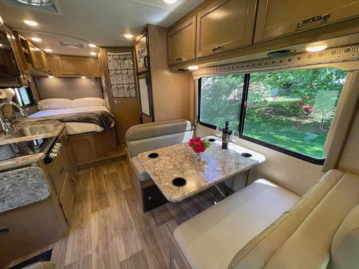 Inside an RV rental, showing the cozy bedroom, functional kitchen, and inviting dinette set for two with a lovely window view.. Thor Motor Coach Four Winds 2019