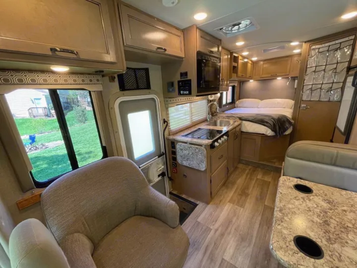Cozy RV rental interior featuring a compact kitchen, comfortable bed, and dinette area, ready for your travel adventures.. Thor Motor Coach Four Winds 2019