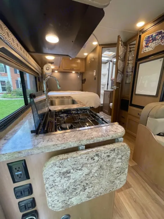 Inside a modern **rv rental**: full kitchen with stove, sink, and ample counter space. Cozy, well-lit travel home interior.. Thor Motor Coach Four Winds 2019