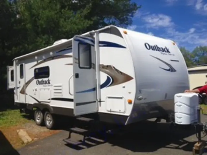 This white Outback travel trailer is an RV rental, parked outdoors with its slide-out extended and door open.. Keystone RV Outback 2011
