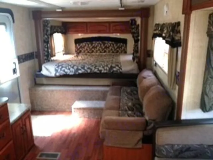 Spacious RV rental interior: raised bed, comfy sofa, and wood floors for your next adventure.. Keystone RV Outback 2011