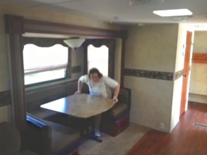 Explore this RV rental's spacious dinette booth with a table, where a woman demonstrates comfortable seating for your road trip.. Keystone RV Outback 2011