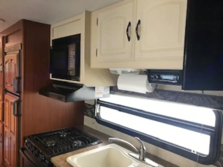 Inside an RV rental: a bright kitchen with microwave, stovetop, sink, and ample cabinets by a window.. Keystone RV Outback 2011