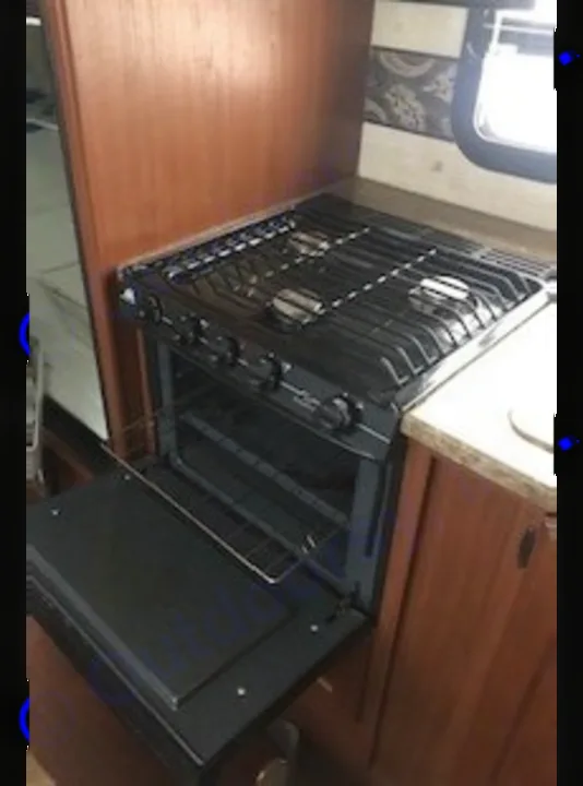 Cooking made easy in your RV rental with this compact black propane stovetop and oven. The oven door is open, showing the rack.. Keystone RV Outback 2011