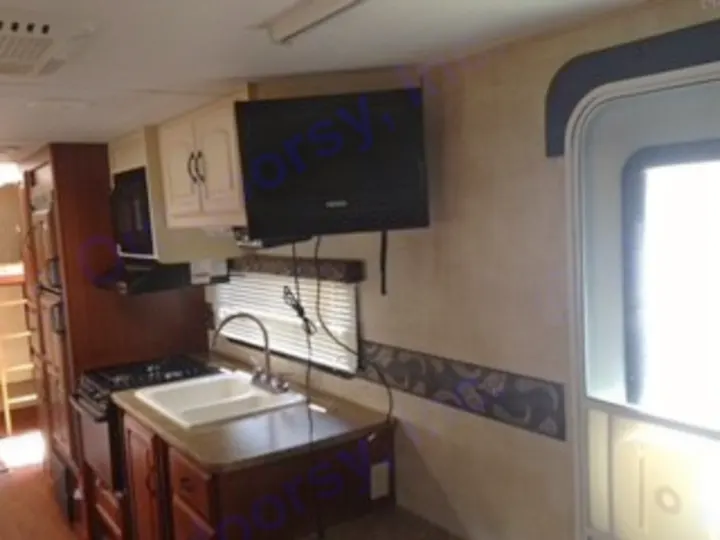 Interior of a modern RV rental, showing a kitchen with sink, stove, microwave, cabinets, and wall-mounted TV. Perfect for road trips.. Keystone RV Outback 2011