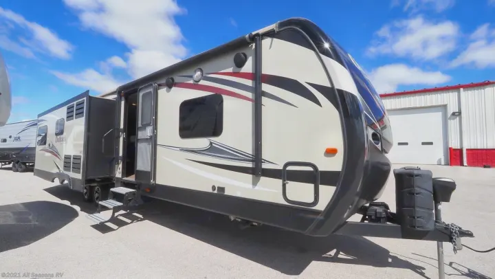 Modern travel trailer, great for rv rental. Beige with graphics, open door, and extended slide-out on a sunny day.. Keystone Outback 2016