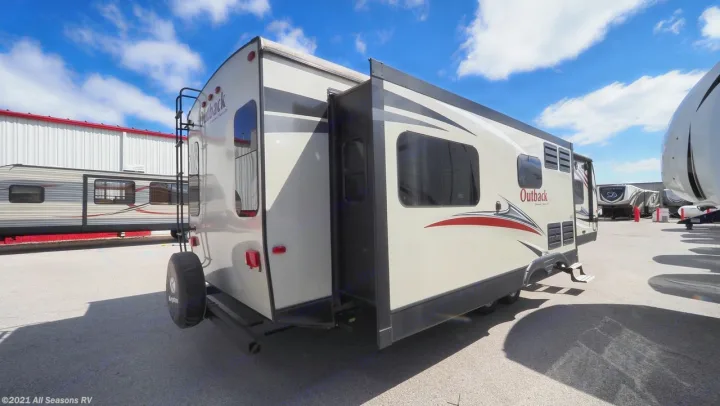 Light-colored Outback RV rental, a travel trailer with an open slide-out, ready for adventures on a sunny lot.. Keystone Outback 2016