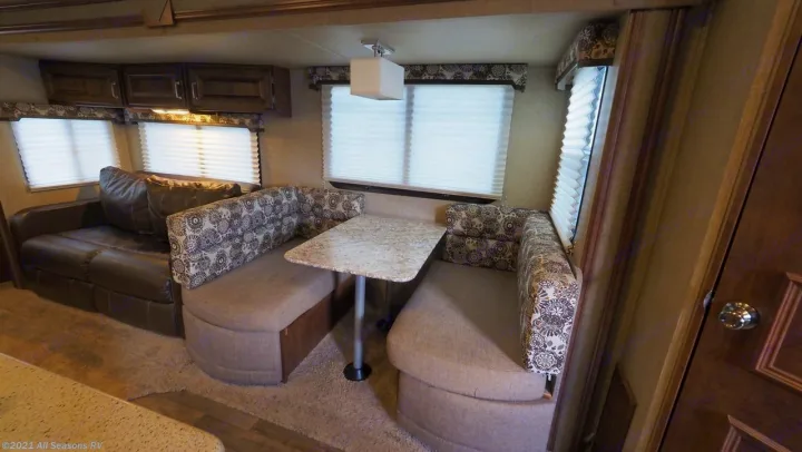 RV rental interior features a brown sofa, patterned dinette, and large windows, creating an ideal camper living area.. Keystone Outback 2016