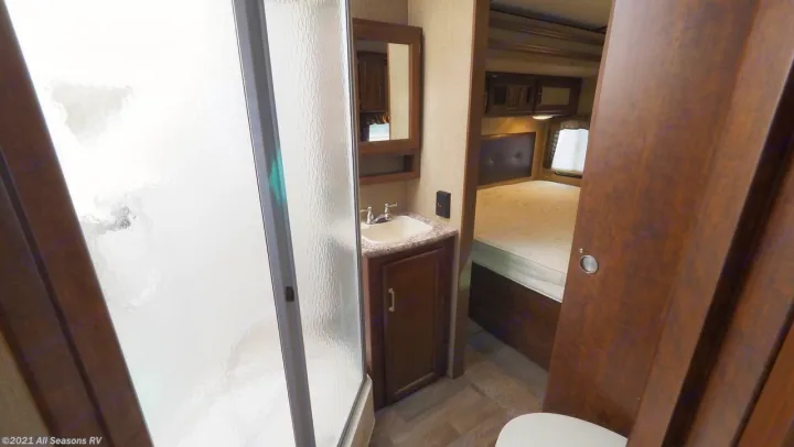 Compact RV rental interior featuring a bathroom with shower, sink, and mirror, leading to a cozy bedroom with a bed.. Keystone Outback 2016
