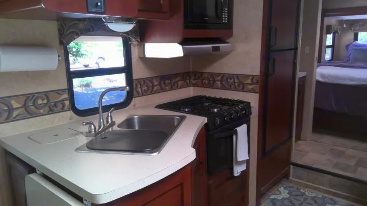 This RV rental offers a well-equipped kitchen area with a sink, stove, microwave, and refrigerator, leading to a bedroom.. Forest River Sunseeker LE 2014