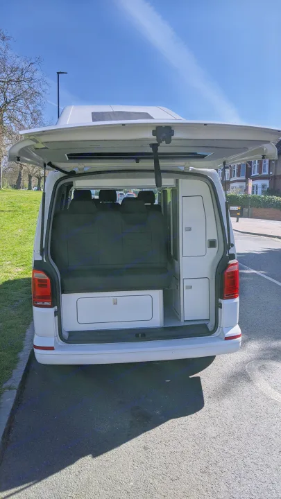 White campervan with open tailgate, revealing interior storage & seats. Perfect for RV rental road trips.. vw T6 2016