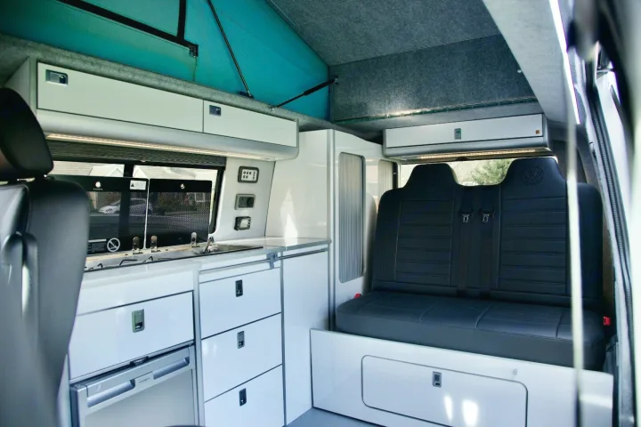 Spacious RV rental interior featuring a modern kitchen with sink, stove, fridge, and rear seating with a pop-top.. vw T6 2016