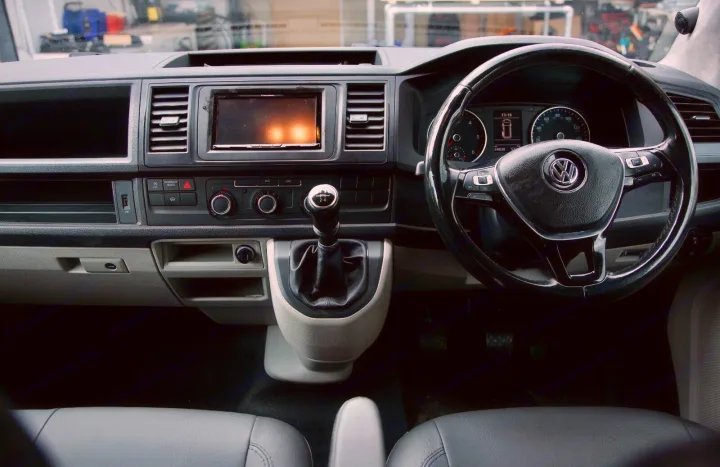 Driver's perspective inside a modern RV rental campervan, showing dashboard, steering wheel, and manual gear stick.. vw T6 2016