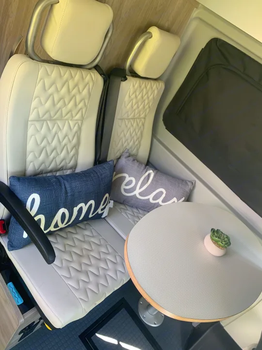 RV rental seating area: white quilted seats, "home" & "relax" pillows, round table with plant, textured floor.. Winnebago Winnebago 2021