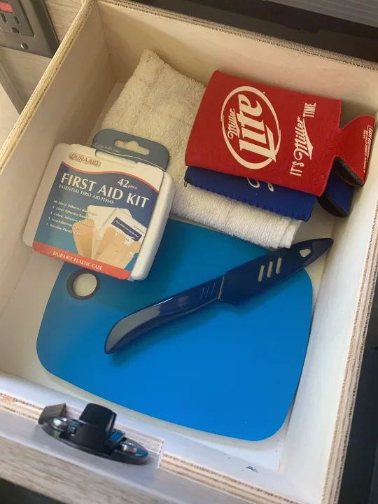 A well-stocked drawer in an RV rental with a first aid kit, cutting board, knife, and drink koozies for travel essentials.. Winnebago Winnebago 2021