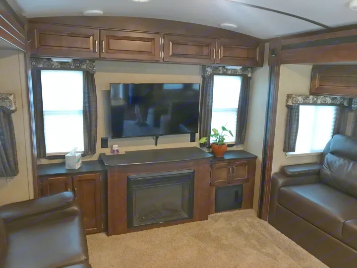 Spacious RV rental interior: living room with TV, fireplace, cabinetry, and brown leather seating.. Keystone Outback 2018