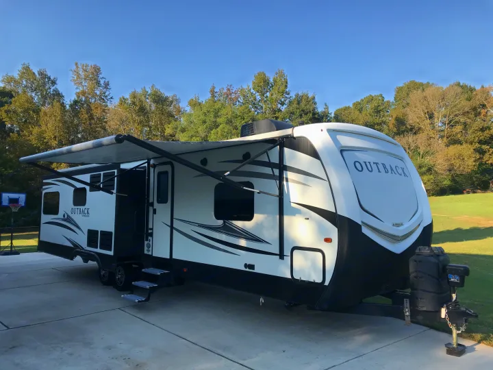 White Outback travel trailer with awning extended, parked on concrete. Ideal for an RV rental adventure.. Keystone Outback 2018