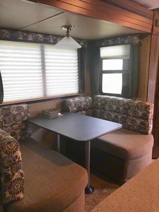 A cozy RV rental dinette featuring patterned U-shaped bench seating, a dark table, and window blinds.. Keystone Outback 2018