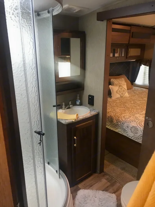 Cozy RV rental interior featuring a compact bathroom with shower and vanity, adjacent to a comfortable bedroom area.. Keystone Outback 2018